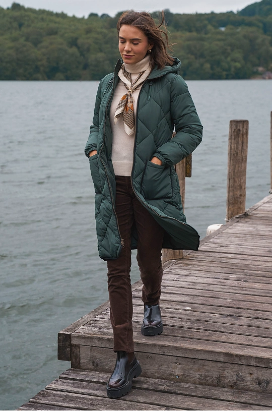 Femme portant un long manteau matelassé et des bottes au bord d'un lac