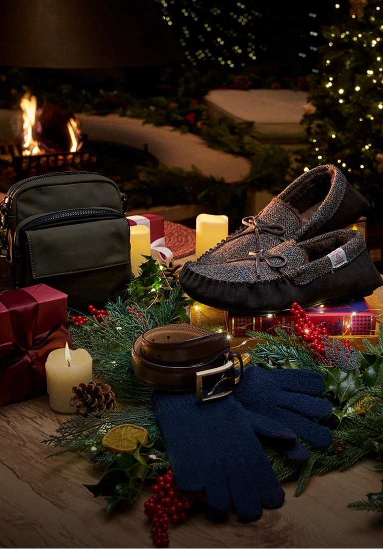 Cadeaux de Noël, notamment un sac, des chaussures, des écharpes et un bonnet bleu, disposés avec de la verdure festive et des bougies