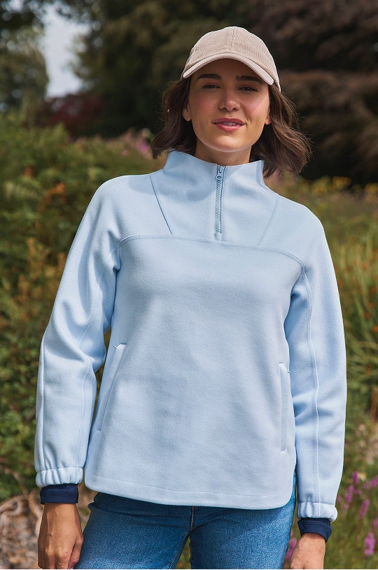 Femme portant un pull bleu clair à col zippé et une casquette en plein air