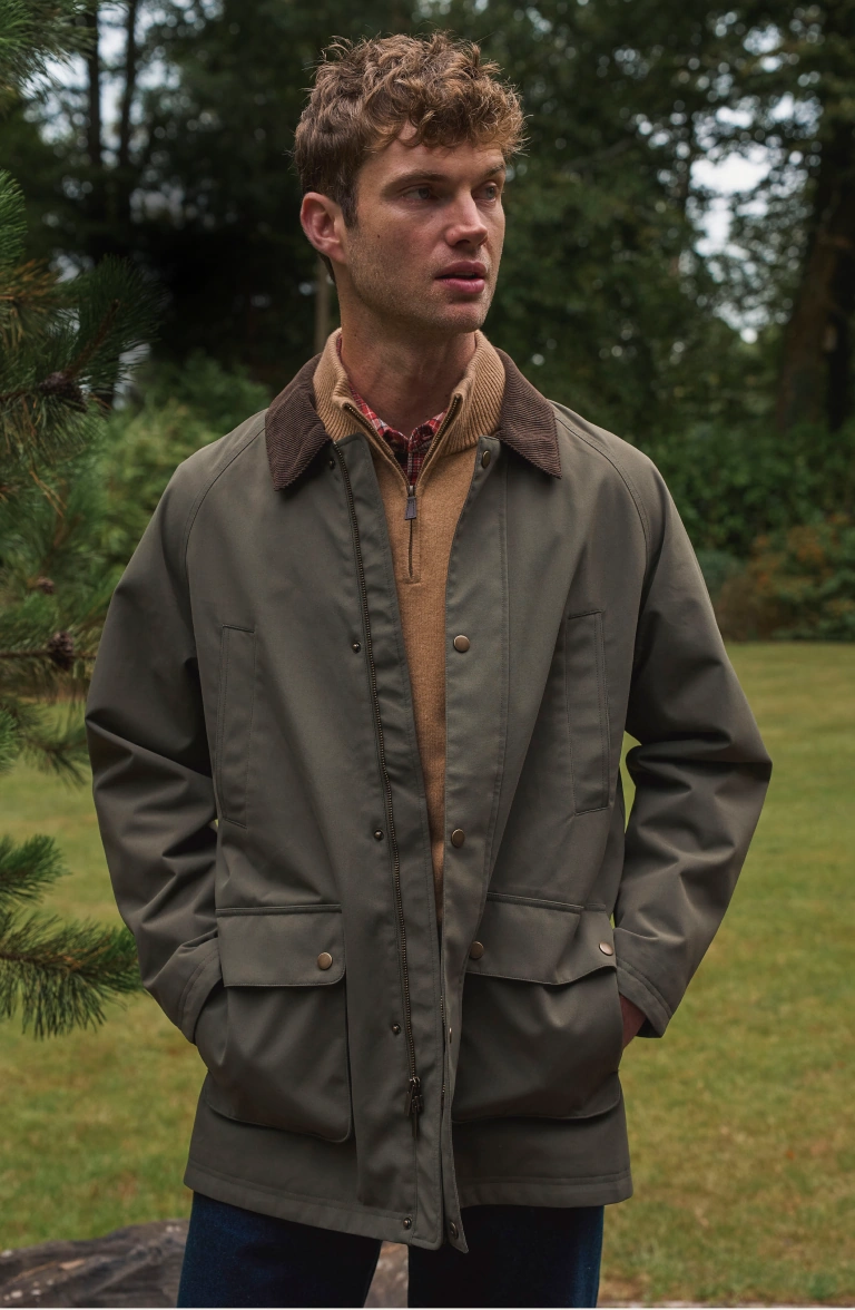 Homme portant une veste cirée, un pull à col zippé et une chemise à carreaux en plein air